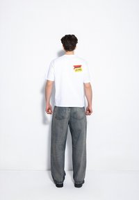 Biała koszulka z krótkim rękawem z kolorową grafiką metki cenowej z tyłu, zestawiona z luźnymi, wyblakłymi niebieskimi dżinsami.