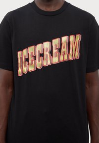 Black cotton t-shirt featuring bold "ICECREAM" text in yellow with red outline and a checkered pattern, round neck, short sleeves.