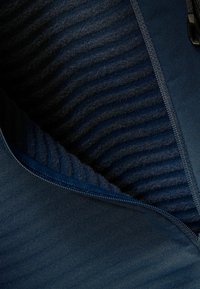 Die marineblaue Jacke mit Reißverschluss verfügt über einen glatten Außenstoff und eine gerippte Innenstruktur, die unterschiedliche Schattierungen von Dunkelblau betont.