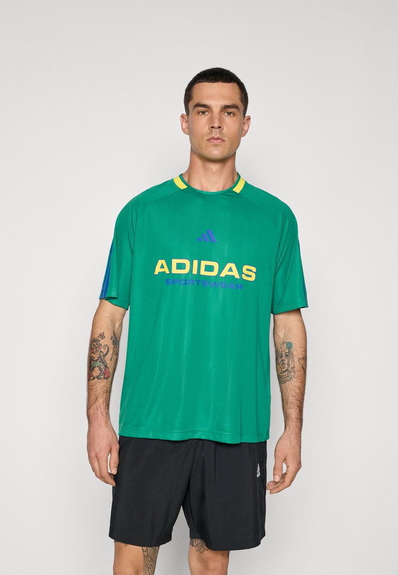 Zöld sportpóló kék és sárga részletekkel, melynek közepén a "ADIDAS SPORTSWEAR" logó megtalálható, vastag sárga és lila betűkkel, lélegző anyagból készült.