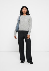 Grijze, gestructureerde gebreide trui met een ronde halslijn, gecombineerd met zwarte wijde broek en een blauwe handtas. Zwarte ballet flats maken de look compleet.