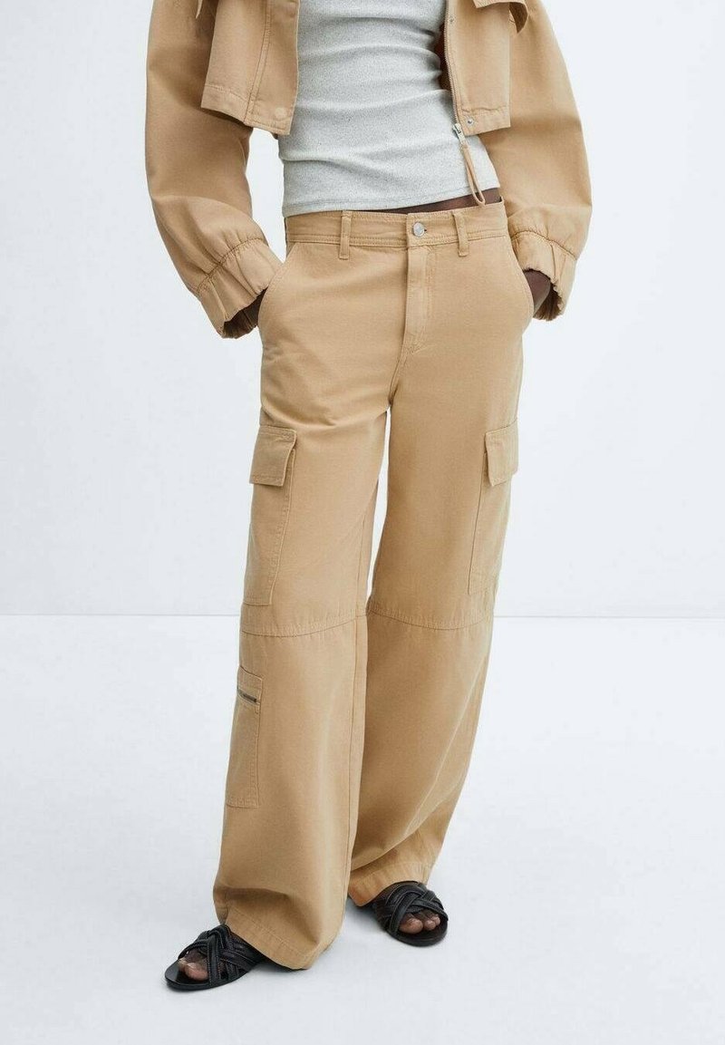 Beige cargobroek met een wijde pasvorm, meerdere zijzakken en een subtiele textuur. Gecombineerd met een aansluitend grijs topje en zwarte sandalen.