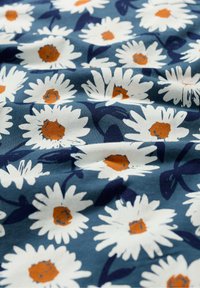 Gėlėta medvilninė medžiaga mėlynu fonu, su baltais ramunėmis oranžiniais viduriais ir tamsiai žaliais lapais, sudarančiais pasikartojantį raštą.