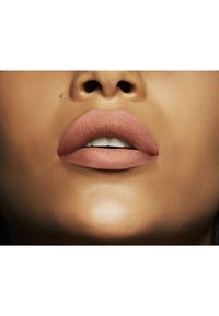 Rouge à lèvres nude mat appliqué sur des lèvres pulpeuses, mettant en valeur une texture lisse et un éclat naturel. Le teint de la peau est chaud, avec des reflets et des contours subtils.