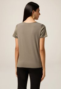 Tricou verde măsliniu cu mâneci scurte, având o textură moale și un decolteu rotund. Detaliu din satin neted, contrastant, pe panoul din spate.