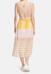 Bezramínková, kolenní šaty v béžovo-růžovo-žlutém batikovaném vzoru s páskem v oblasti pasu a kl íčovou dírkou na zádech. Kombinujte s bílými teniskami.