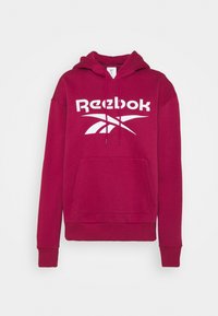 Maroon hoodie med en framficka, ribbad mudd och fåll, med en stor vit Reebok-logga på bröstet. Mjuk, strukturerad ibland.