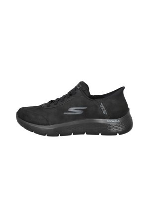 Zapatilla deportiva de ante negra con suela texturizada, diseño con cordones y un logotipo prominente en el lateral. Cuenta con un talón acolchado para mayor soporte.