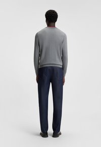 Gray knitted sweater with a round neckline and red accent at the back, paired with dark blue denim pants and black shoes.