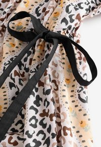 Haljina s leopard uzorkom s crnom trakicom; sadrži pastelne nijanse, leteći materijal s mekom teksturom i ukrasnim cvjetnim uzorcima.