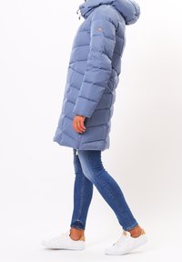 Puffjacka i ljusblått, med huva, vertikalt quiltat mönster och dragkedjestängning. Kombinerad med mörka jeans och vita sneakers.