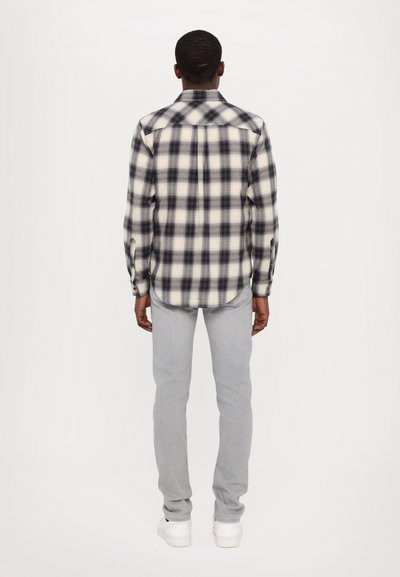 Svartvitt rutigt flanellskjorta med långa ärmar, knäppta manschetter och rundad nederkant, tillsammans med ljusgrå slim fit-jeans.