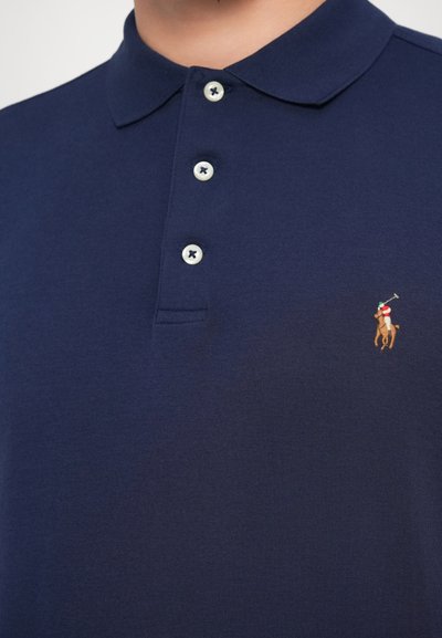 Temno modra polo majica iz bombaža, z trojnim gumbom na zapenjanju, mehko teksturo in izvezenim logotipom igralca polokluba na prsih.