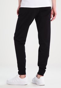 Black jogger pants made of cotton blend, featuring cuffed ankles and side pockets, paired with white sneakers on a plain background.