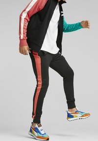 Track jacket with red, black, and teal colors, paired with black pants featuring coral side stripes. Colorful sneakers with multiple accents.