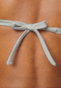 Fita branca texturizada amarrada em um laço contra uma superfície de pele suave e bronzeada, destacando o contraste entre as cores e os materiais.