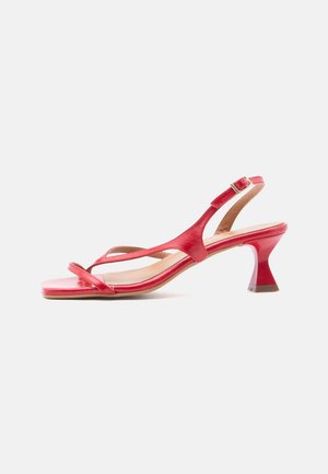 Sandalia tipo slingback de cuero rojo con tacón bajo acampanado, punta cuadrada, tiras delgadas y cierre de hebilla ajustable sobre fondo claro.