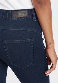 Vaqueros de denim azul oscuro con un parche de logo negro en la cinturilla y un diseño sencillo de bolsillo trasero con costuras limpias.