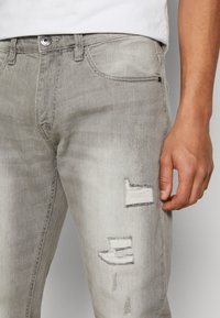 Gray denim jeans featuring a slim fit, distressed patches, and subtle fading. Includes contrast stitching and a side pocket design.
