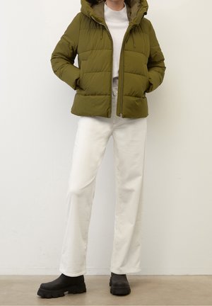 Olivenfarvet dunjakke med hætte, lynlås foran og elastiske snore. Kombineret med hvide bukser med brede ben og sorte chunky støvler.