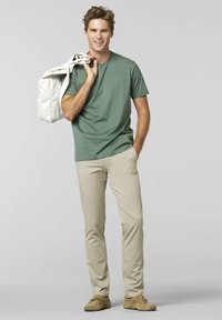 Groene korte mouwen t-shirt, beige slim-fit broek, met een witte tote bag. Schoenen zijn bruin met een zachte textuur. Eenvoudig ontwerp, geen patronen.