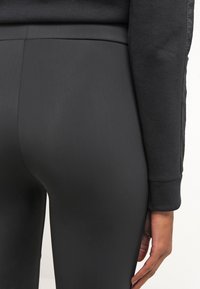 Svarta leggings gjorda av elastiskt material, med hög midja och en slät textur; närbild som framhäver passform och silhuett.