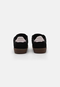 Black suede sneakers with a brown rubber outsole, featuring padded cuffs and a smooth upper. Minimalistic design, stitched detailing.