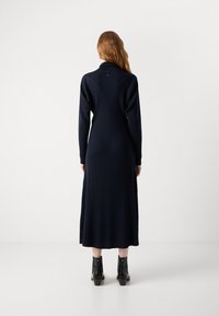 Vestido de manga larga en color navy con textura acanalada, diseño de espalda en forma de V y aberturas laterales. Combinado con botines negros hasta el tobillo.