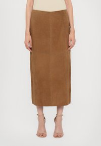 Brun mockask midi kjol med en åtsittande midja, rena linjer och kontrasterande sömmar. Buren med ljusfärgade sandaletter.