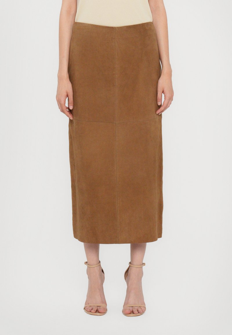 Brun mockask midi kjol med en åtsittande midja, rena linjer och kontrasterande sömmar. Buren med ljusfärgade sandaletter.