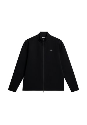 Musta vetoketjullinen takki, jossa on pystykaulus ja joka on valmistettu teksturoidusta materiaalista. Takissa on hienovarainen logo vasemmassa rinnassa ja pitkät, suorat hihat.