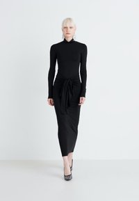 Μαύρο μακρύ μανίκι φόρεμα με εφαρμοστή σχεδίαση, που διαθέτει σφιχτό κόμπο στη μέση. Φτιαγμένο από ομαλό, ελαφρώς ελαστικό ύφασμα.