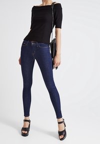 Top negro sin mangas con rayas texturizadas, combinado con jeans ajustados azul oscuro y tacones de plataforma negros. Incluye un pequeño bolso cruzado negro.