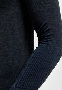 Zwarte sportieve longsleeve met een textuur patroon op de mouwen, voorzien van een gladde stof voor het lichaam en schuine zijnaad.