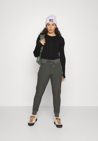 Black long-sleeve top, olive green cargo pants with adjustable drawstring, cream and black hiking shoes, purple knit beanie, green backpack.