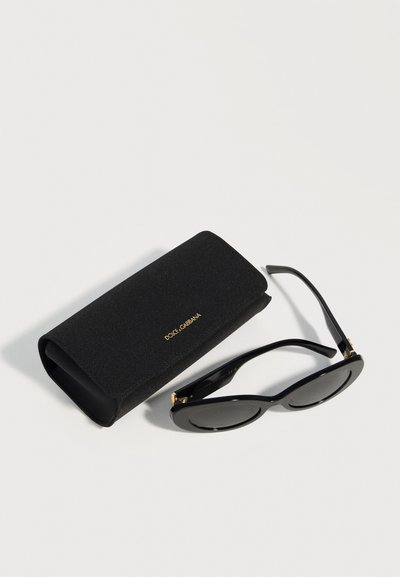 Μαύρα οβάλ γυαλιά ηλίου Dolce & Gabbana με ταιριαστή μαύρη υφασμάτινη θήκη με χρυσό λογότυπο πάνω σε λευκή επιφάνεια.