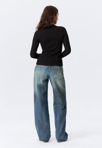 Haut noir à manches longues associé à un jean ample bleu clair délavé, présentant un design classique à cinq poches et une coupe droite.