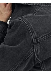 Black denim jacket featuring a textured finish, with visible stitching details and a slightly oversized fit around the shoulders.