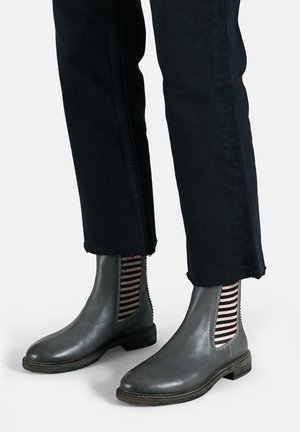 Stivali alla caviglia in pelle grigia con pannelli laterali elastici a righe nere e bianche, posizionati su jeans neri a vita corta con orli sfrangiati.