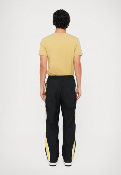 Μαύρο παντελόνι με κίτρινες ρίγες στο πλάι, ελαστική μέση και πλαϊνές τσέπες; σε συνδυασμό με μπλε κοντομάνικο μπλουζάκι. Πίσω άποψη.