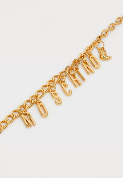 Kuldse tooniga metallketiga käevõru, millel on tähekaunistused sõnaga "MOSCHINO" ja väike dekoratiivne ripats, mis meenutab kinga. Sile ja läikiv viimistlus.