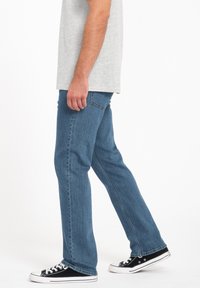 Light blue denim jeans with a straight-leg design, featuring a classic five-pocket layout and stitched detailing. Paired with black sneakers.