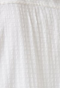 Tessuto bianco strutturato con un motivo a griglia, caratterizzato da una qualità leggera e ariosa e una superficie morbida. Adatto per abbigliamento casual o formale.