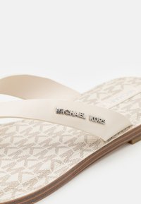 Beežid flip-flop sandaalid, mille jalaplal on tekstuuriga muster. Paindlikud rihmad, millel on reljeefne "Michael Kors" logo, kerge pruuniga tald.