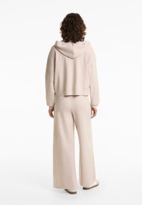 Beige loungewear szett, amely egy kapucnis, rövidített pulcsit és bő szárú nadrágot tartalmaz. Puha, texturált anyagból készült, laza szabással és minimális részletezéssel.