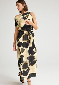 Blomsterpræget maxikjole i beige og sort, med off-shoulder design, bælte ved taljen og flydende stof.