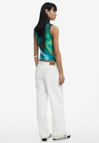 Fitted, sleeveless top in blue-green gradient, paired with loose, white wide-leg jeans featuring a brown label on the waistband.