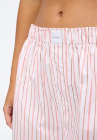 Lähivaade inimese vöökohale, kes kannab roosa-valge triibulise Calvin Kleini kummiga vööpüksid.