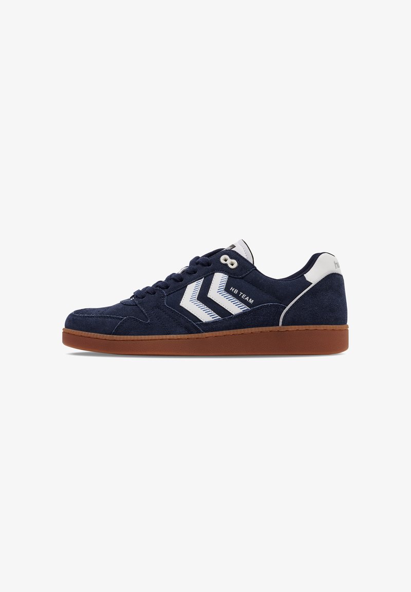 Adidași din suede albastru-navy cu dungi albe de accent, șireturi rotunde și talpă din cauciuc maron. Prezintă o limbă și un călcâi căptușiți pentru confort.