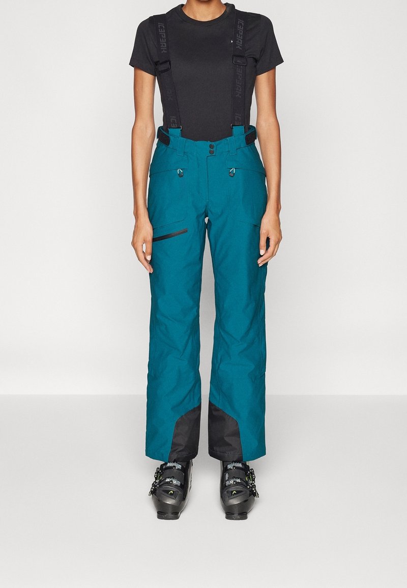 Teal ski pants with black accents, adjustable straps, zippered pockets, and a loose fit. Made from textured, weather-resistant material.